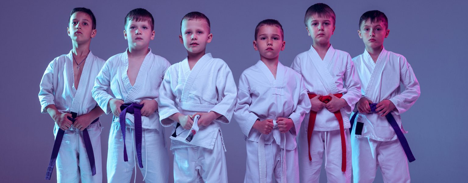 Group of boys, children training martial arts, karate isolated over purple studio background in neon.